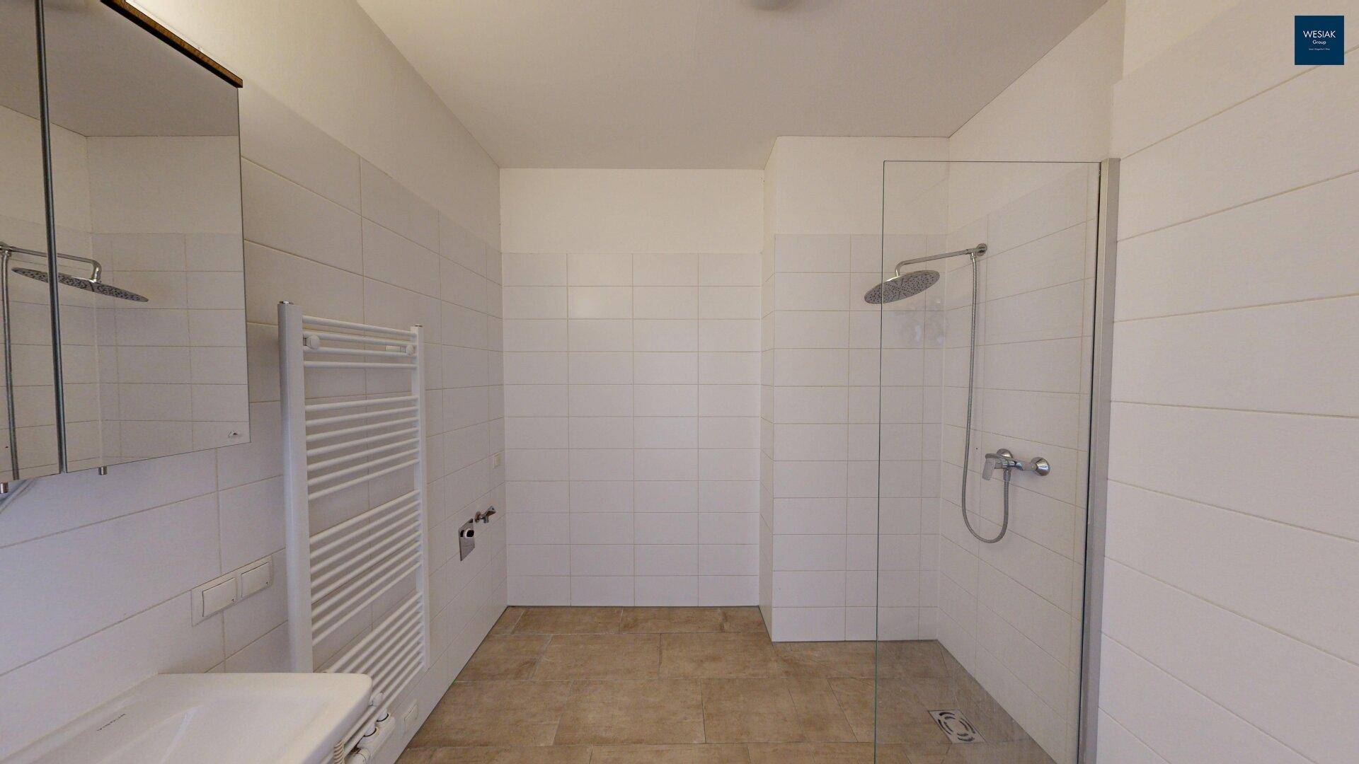 Helles Badezimmer mit begehbarer Dusche, Glasabtrennung und weißen Wandfliesen.