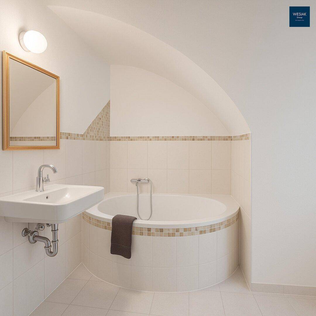 Badezimmer mit runder Eckbadewanne, Waschbecken und hellen Fliesen, unter einer Dachschräge.