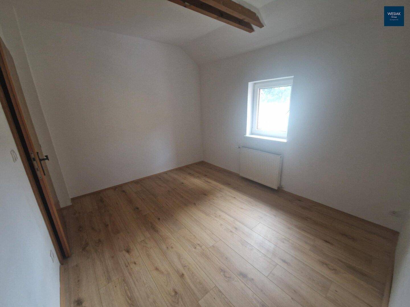 Helles Zimmer mit Laminatboden, einem Fenster und einer Holztür.