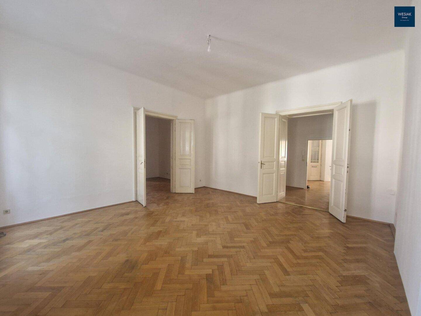 Geräumiges Wohnzimmer mit Fischgrätparkett, hohen Decken und mehreren Flügeltüren, die Räume verbinden.