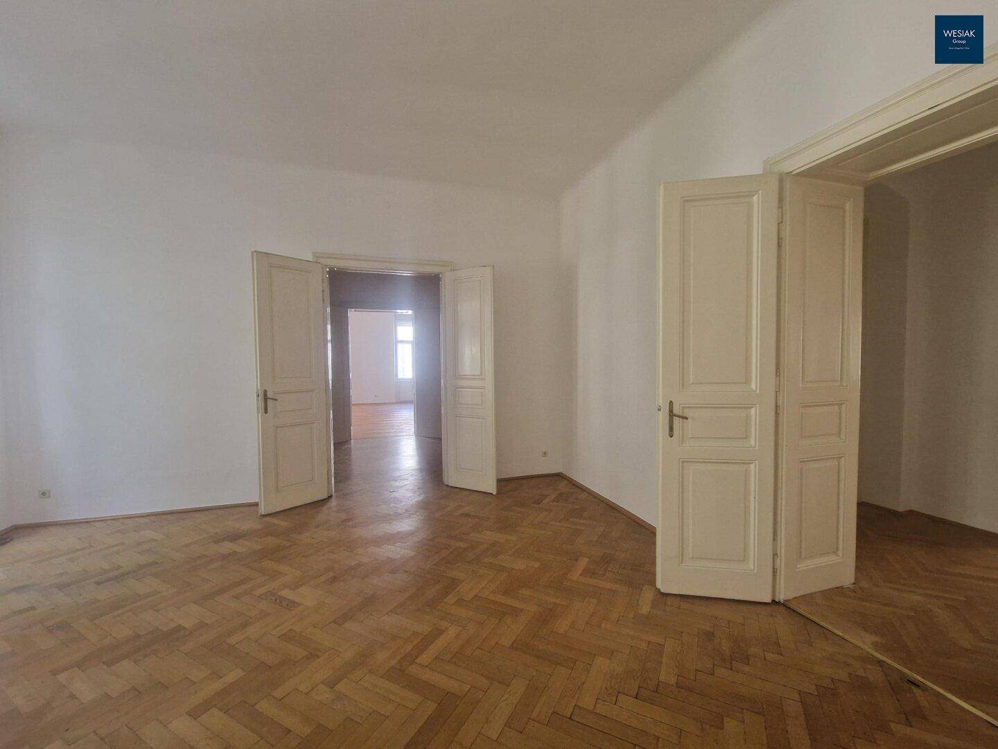 Helles Wohnzimmer mit klassischem Fischgrätparkett und hohen Flügeltüren, die weitere Räume verbinden.