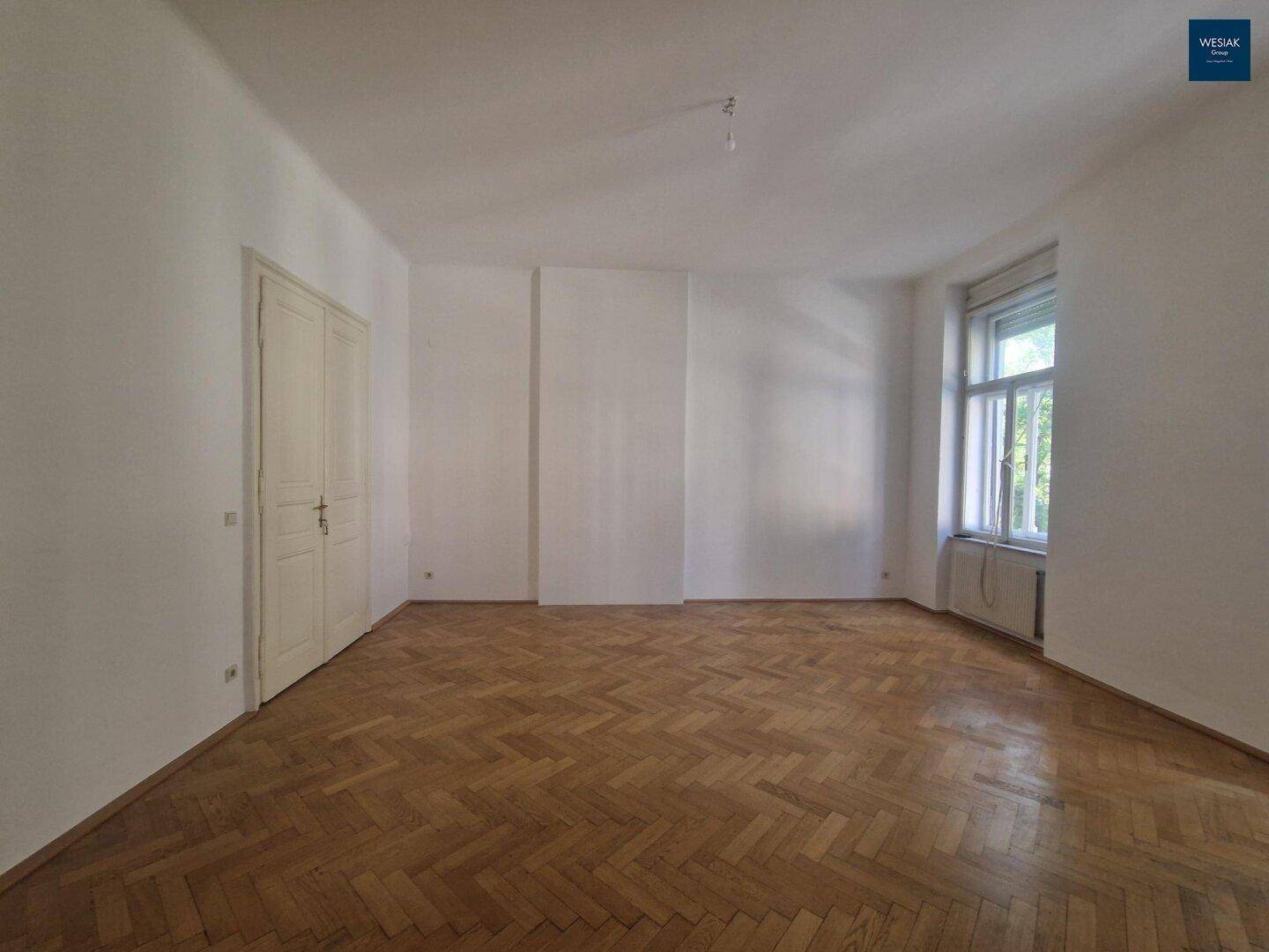 Geräumiges Zimmer mit Fischgrätparkett, hohen Decken und großen Fenstern für viel Licht und Weitblick.