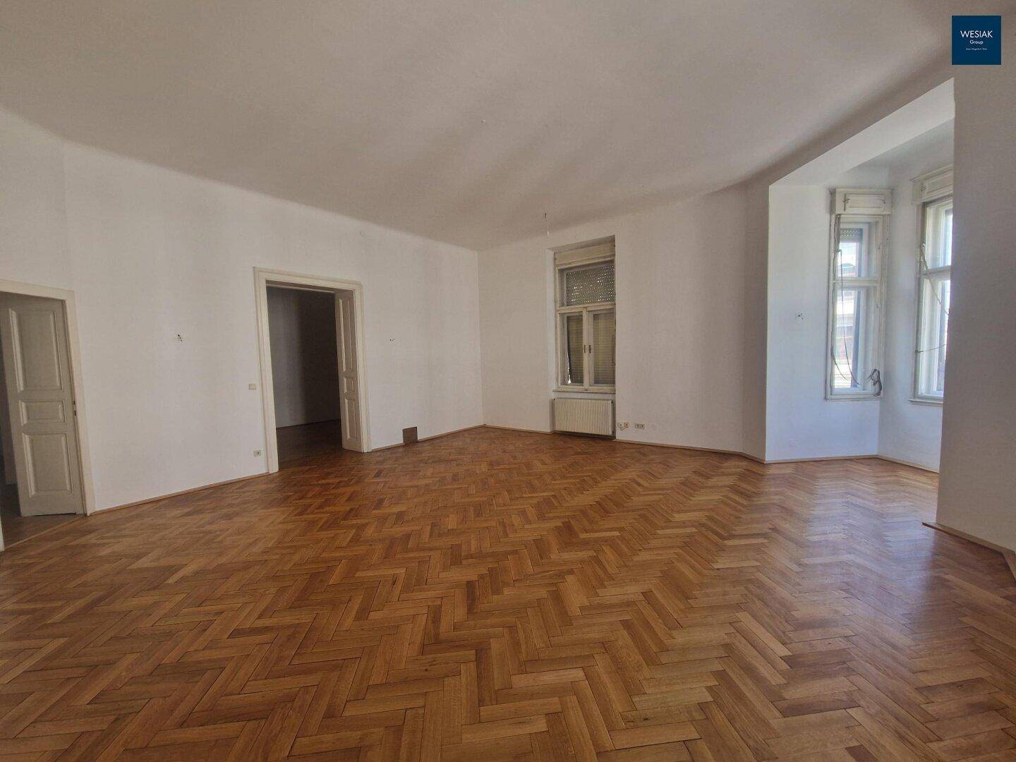 Helles Zimmer mit Fischgrätparkett, hohen Decken und großen Fenstern, die einen weiten Blick bieten.