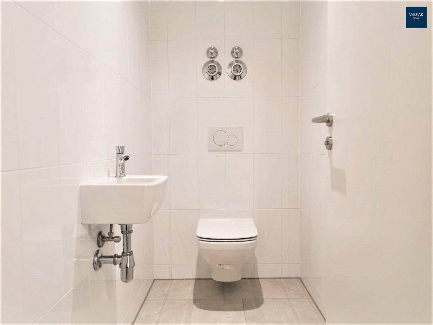 Helles Gäste-WC mit weißen Fliesen, wandhängendem WC und kleinem Handwaschbecken.