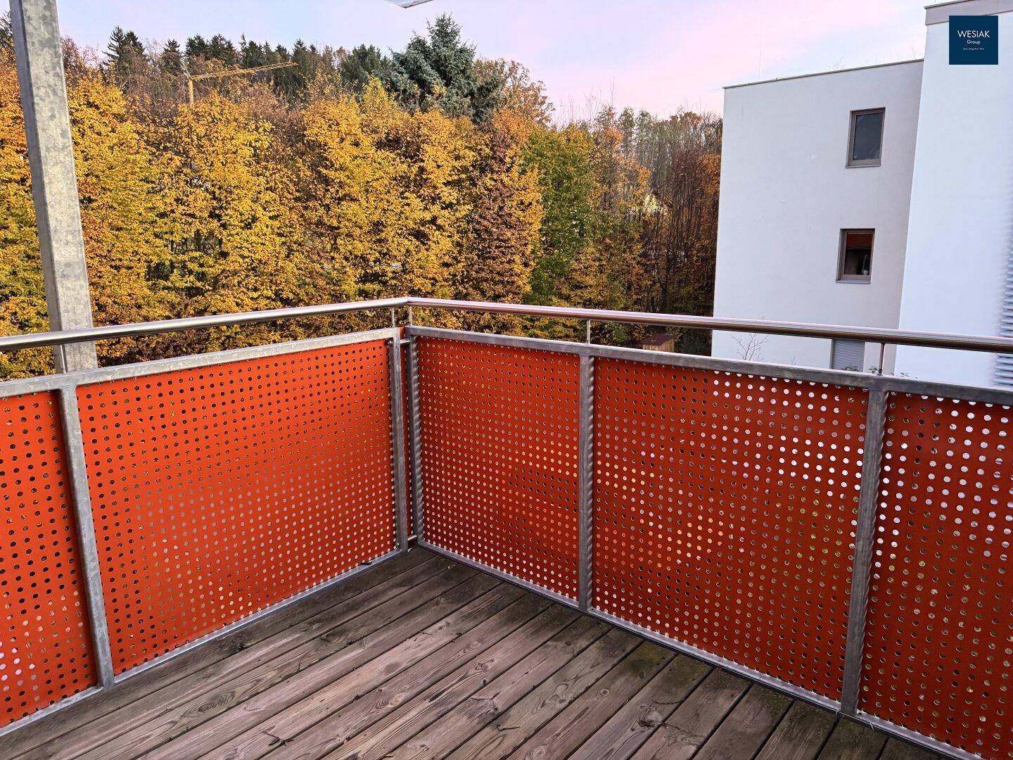 Balkon mit Holzboden und orangefarbenen Lochblech-Geländern mit weitem Blick ins Grüne.