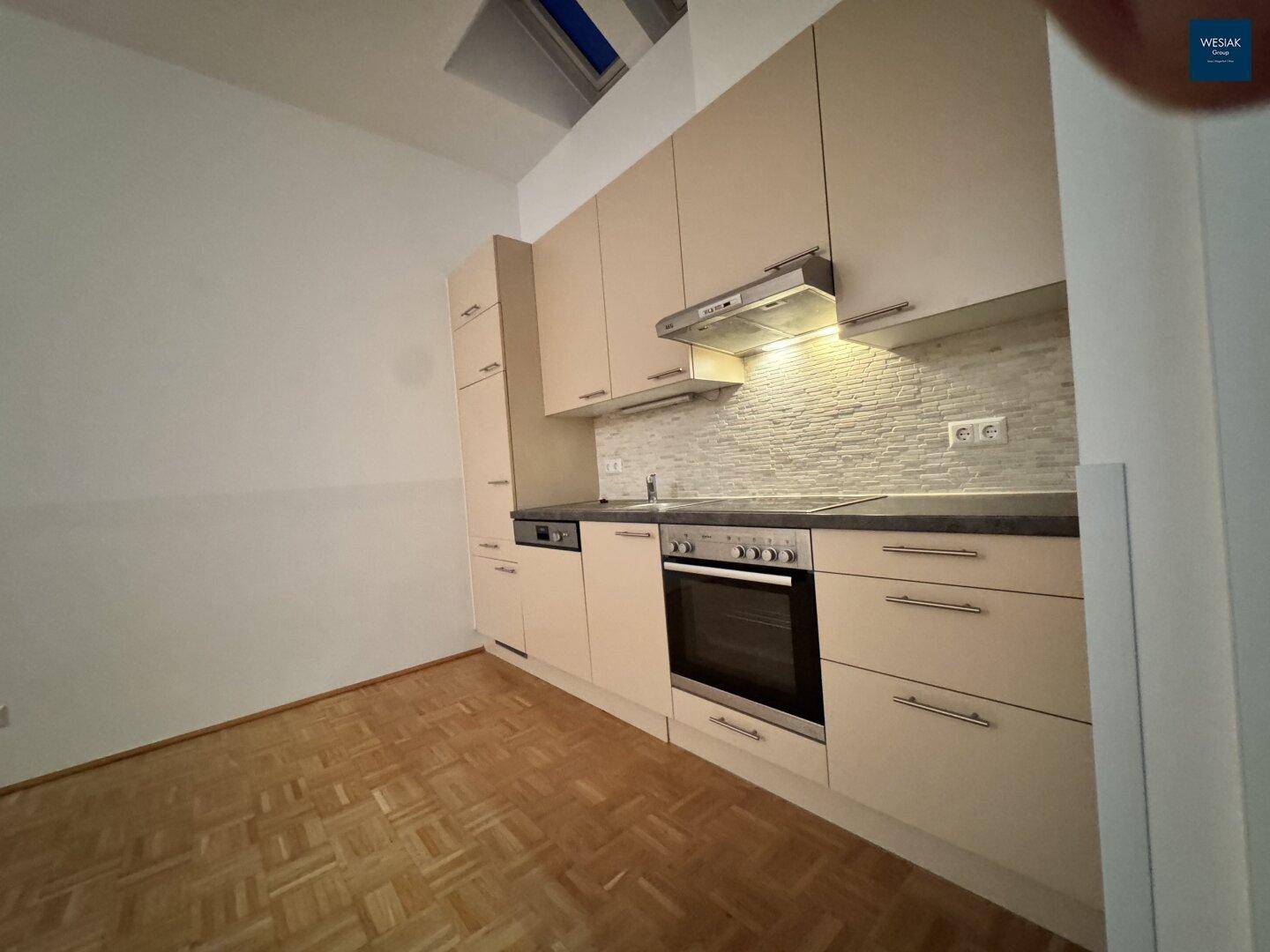 Einbauküche mit beigefarbenen Schränken, integriertem Backofen und Dunstabzugshaube über dem Kochfeld.