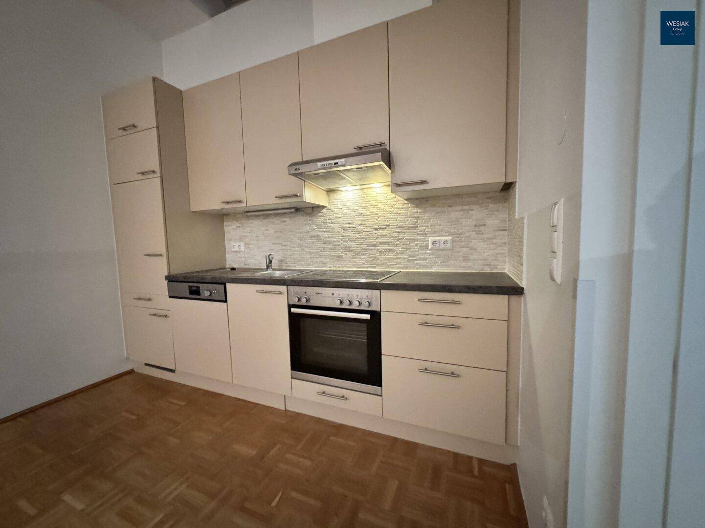 Moderne Einbauküche mit beigefarbenen Schränken, dunkler Arbeitsplatte und integrierten Geräten.