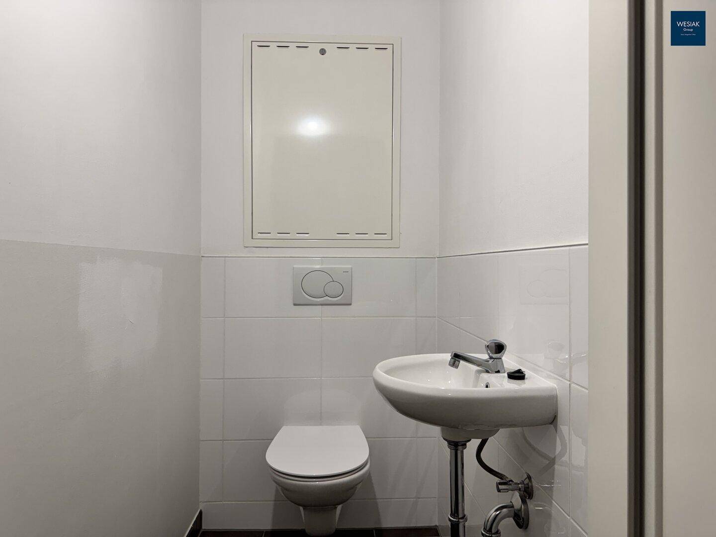 Kleines Gäste-WC mit Wand-WC, Waschbecken und weißen Fliesen im unteren Bereich.