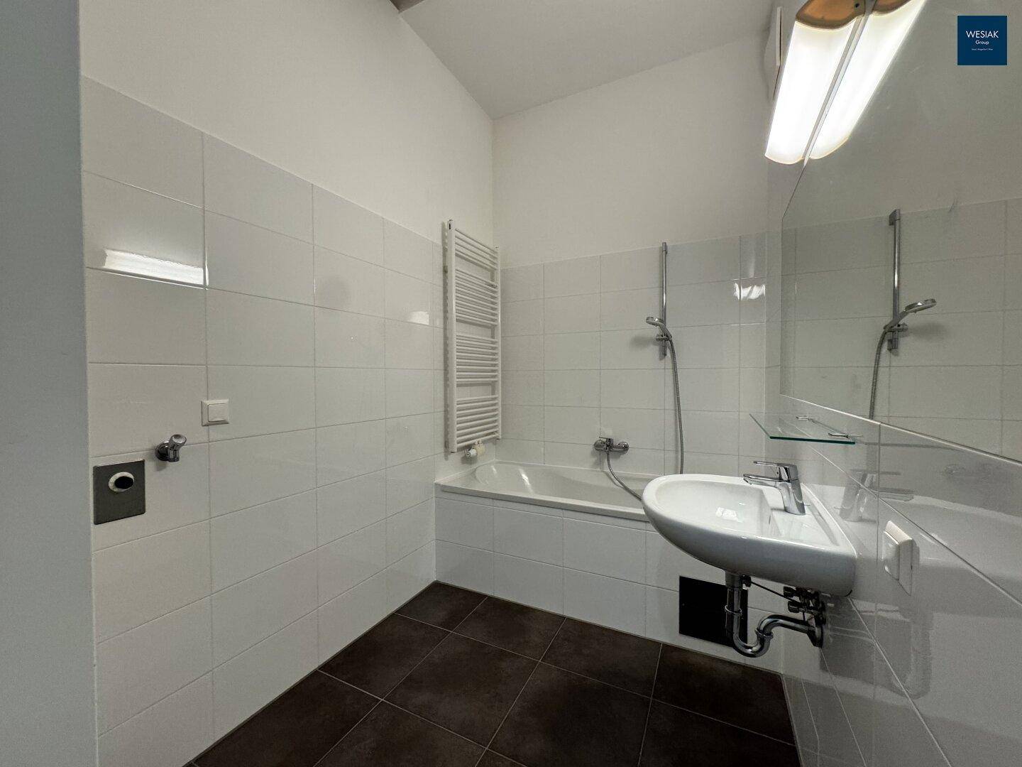 Badezimmer mit Badewanne, integrierter Dusche, Waschbecken und beheiztem Handtuchhalter.