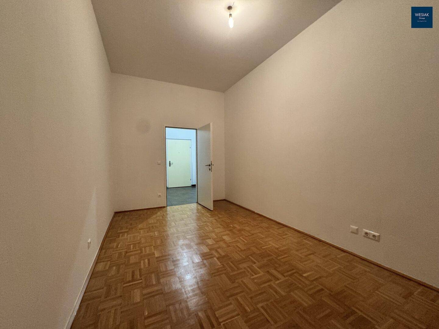 Geräumiges Zimmer mit Parkettboden und einer offenen Tür, die den Zugang zu einem Flur ermöglicht.