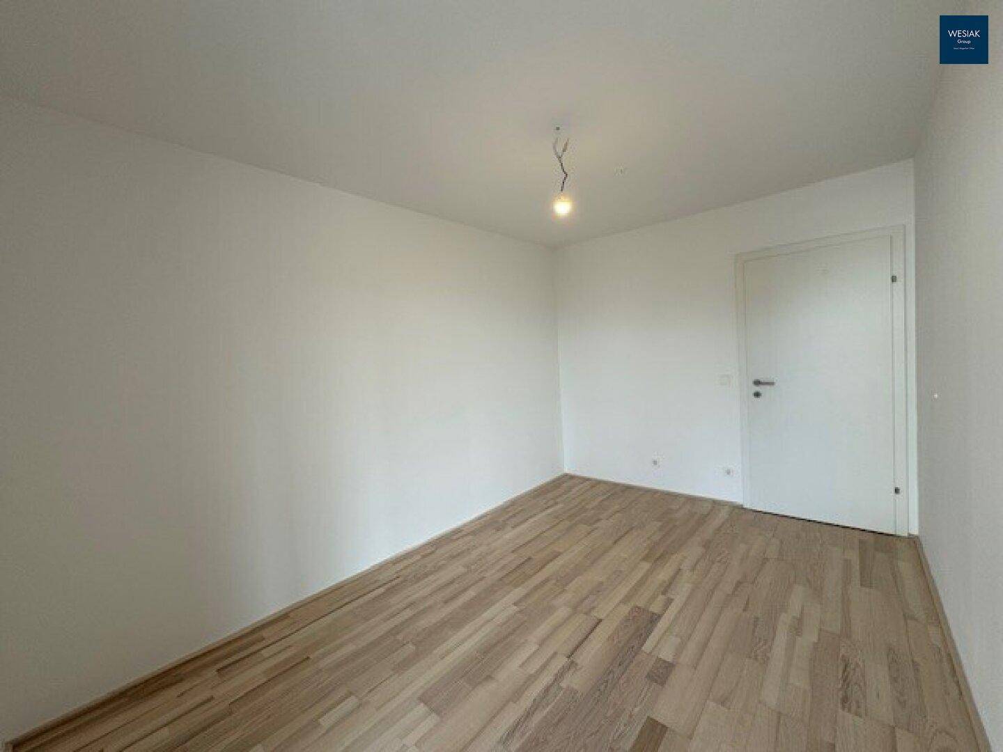 Leeres Zimmer mit hellem Laminatboden und weißen Wänden, bereit zur individuellen Gestaltung.