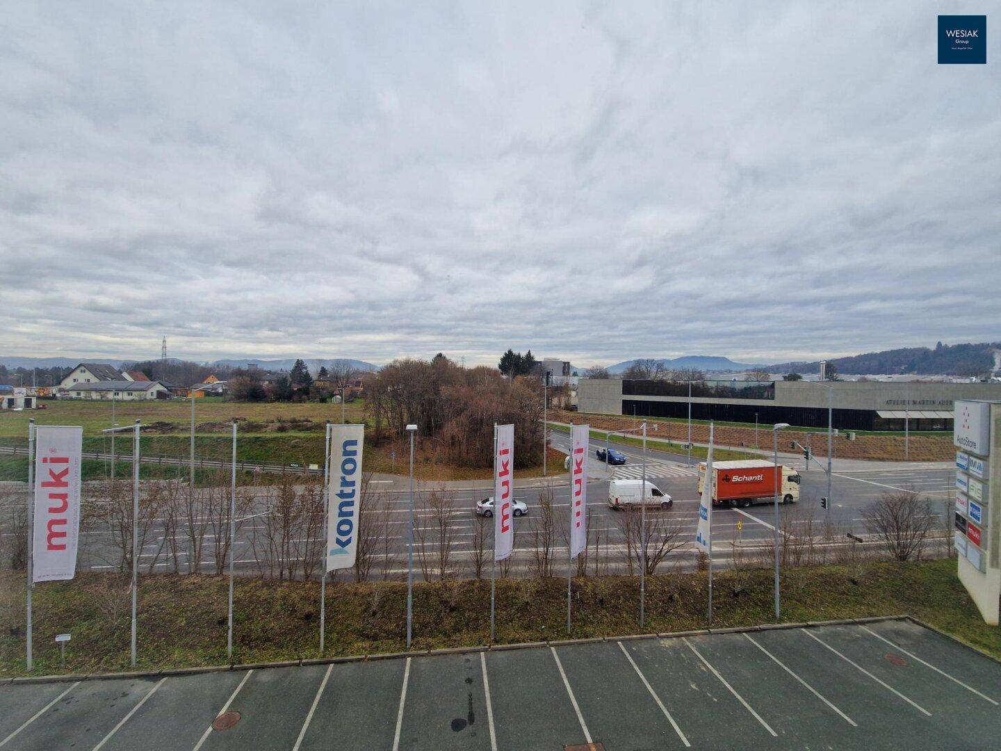 Weitläufiger Blick auf eine Straße, Parkplätze und umliegende Gebäude unter bewölktem Himmel.