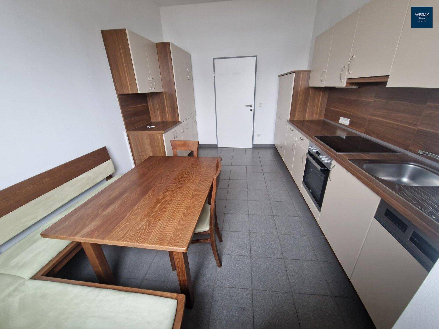 Funktionale Küche mit Fliesenboden, Holztisch und Einbauschränken in Holz- und Beigetönen.