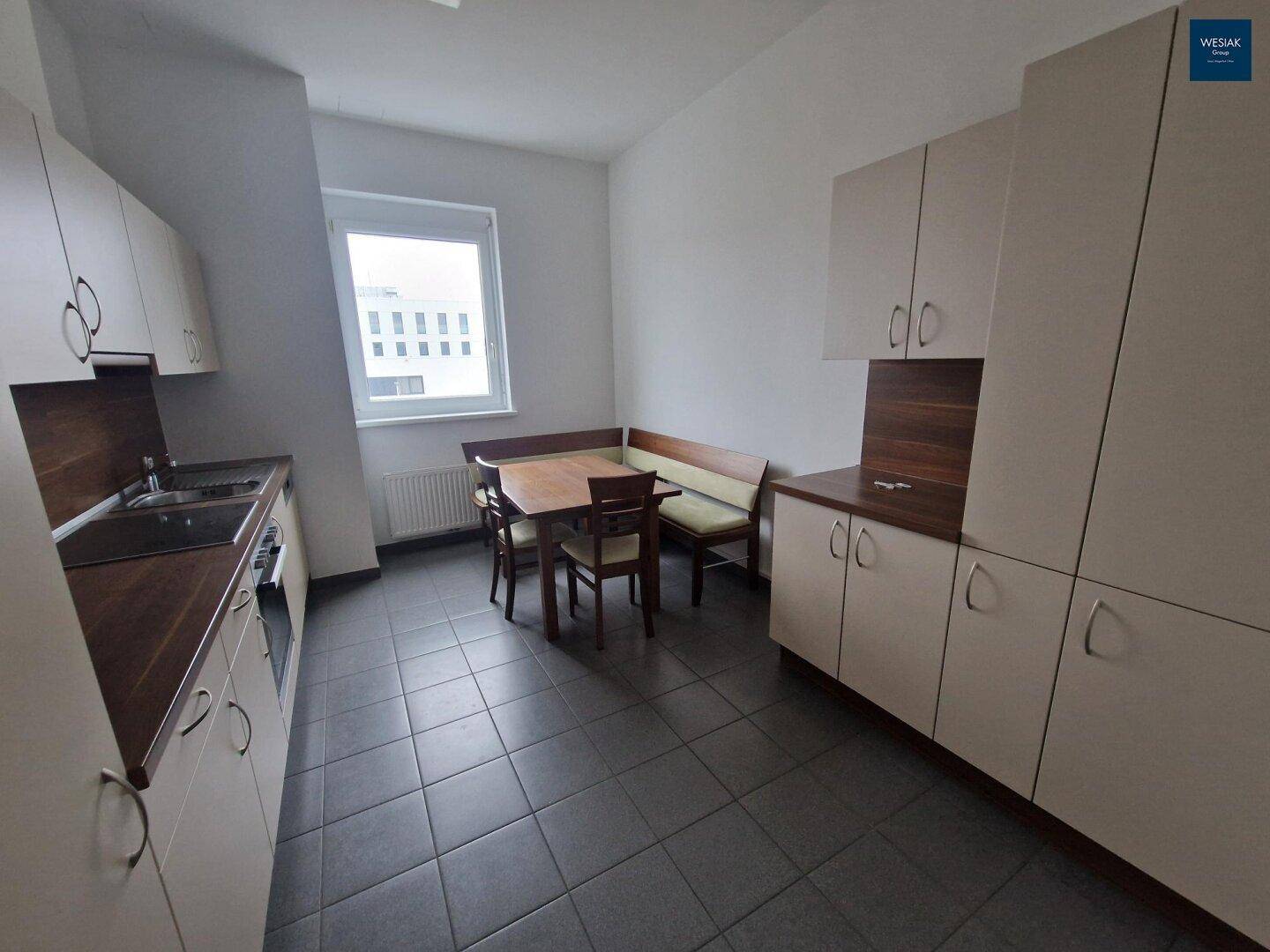 Helle Küche mit Fliesenboden, Essbereich am Fenster und Einbauschränken in Beige und Holz.