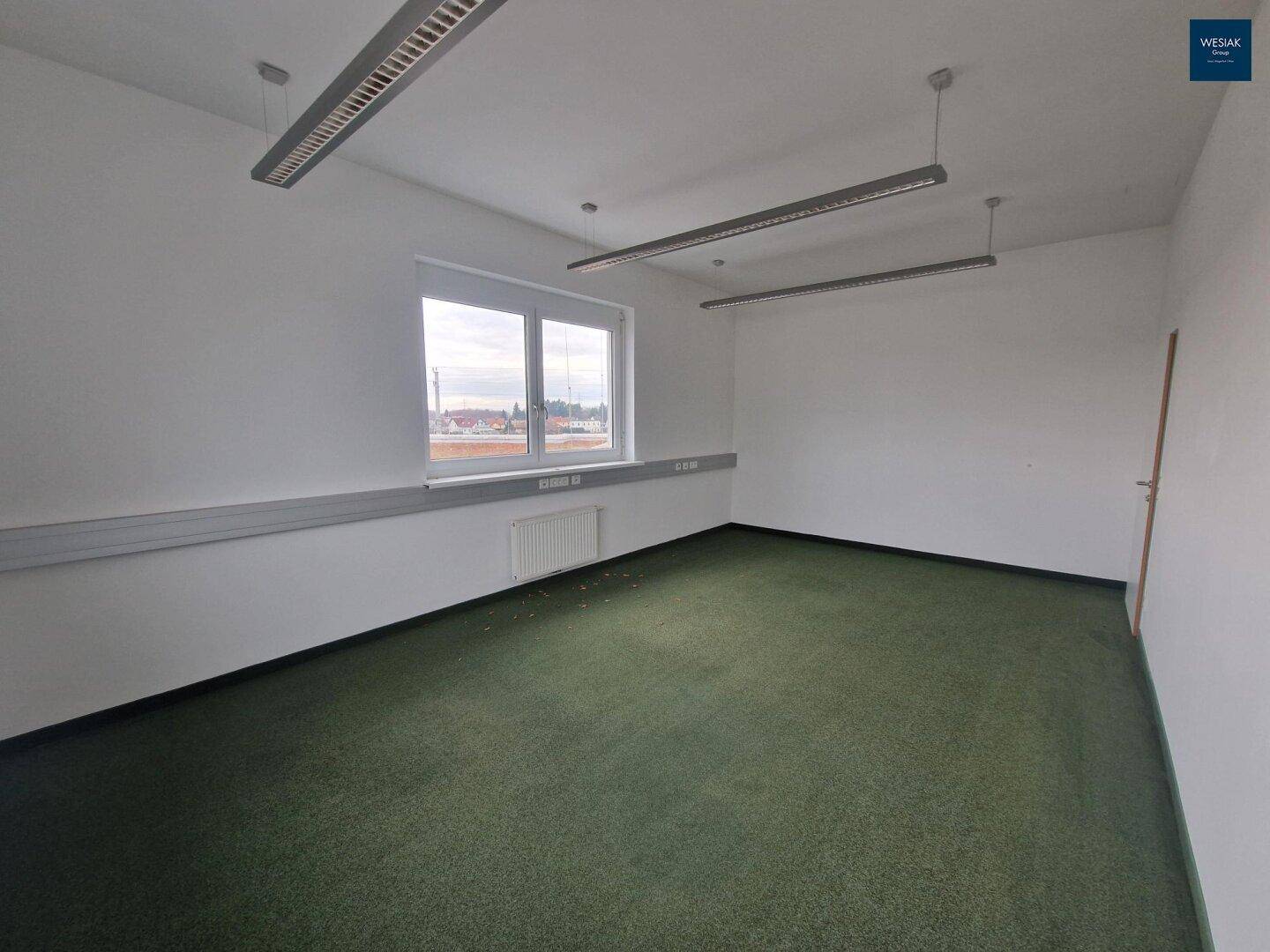 Leeres Büro mit Teppichboden, einem Fenster und Blick auf die Landschaft.