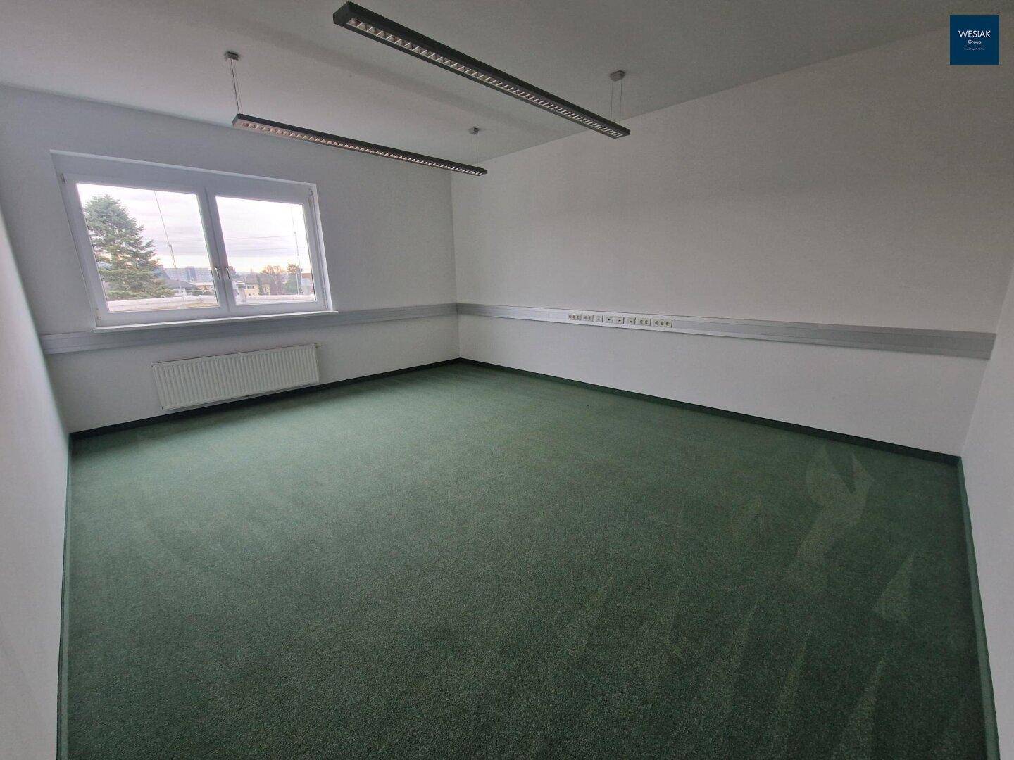 Leeres Büro mit Teppichboden, einem Fenster und Blick auf die Umgebung.