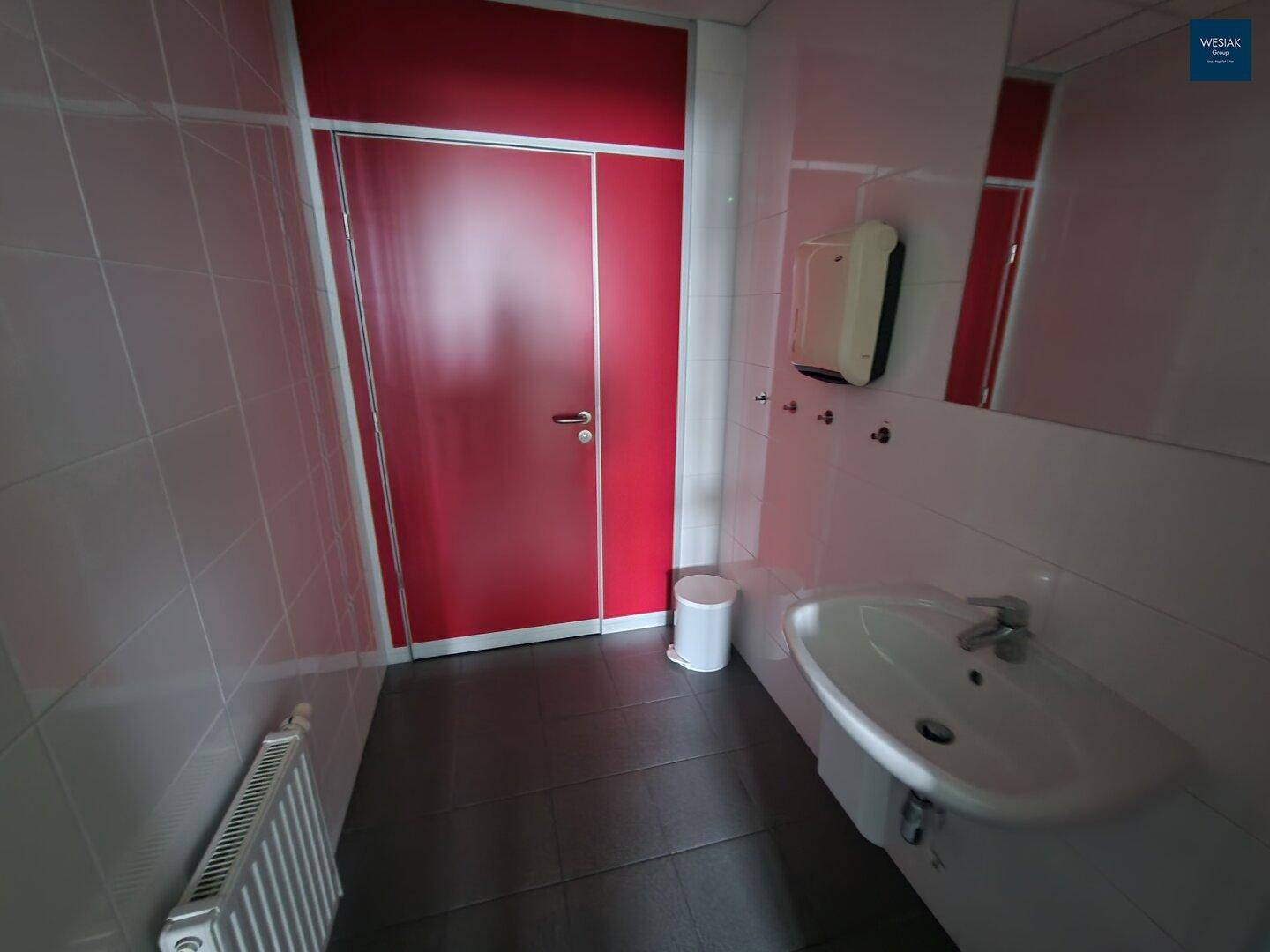 Badezimmer mit Fliesenboden, Waschbecken und einer auffälligen roten Tür.