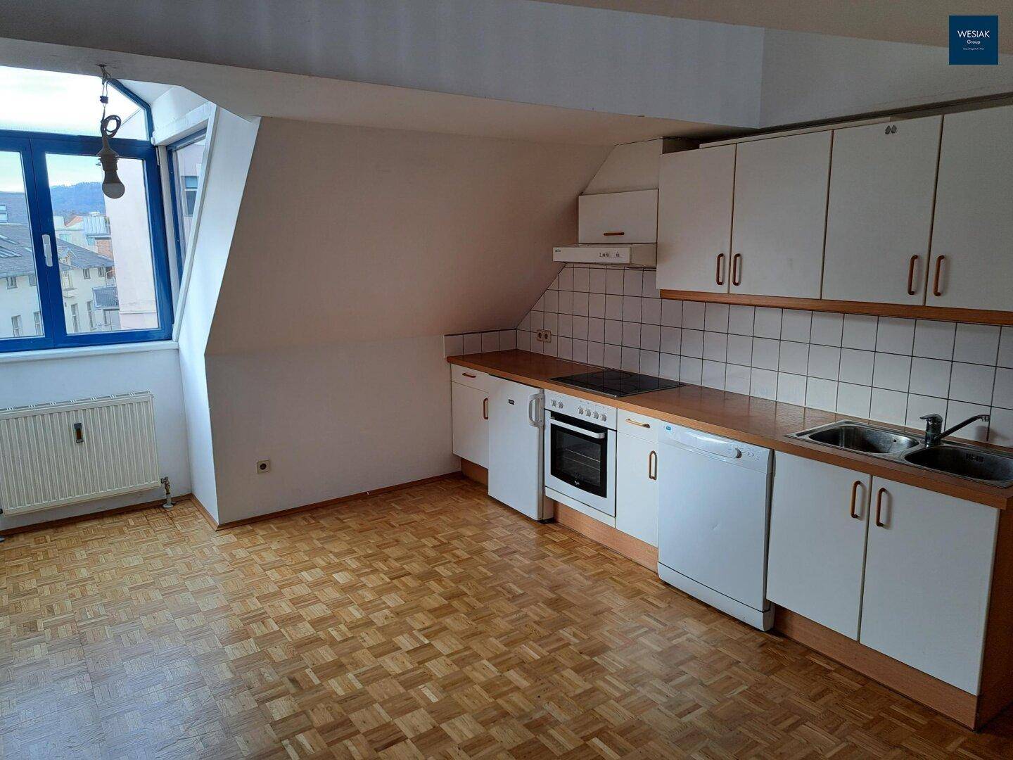 Kleine Einbauküche im Dachgeschoss mit Herd, Spüle und weißen Schränken unter der Dachschräge.