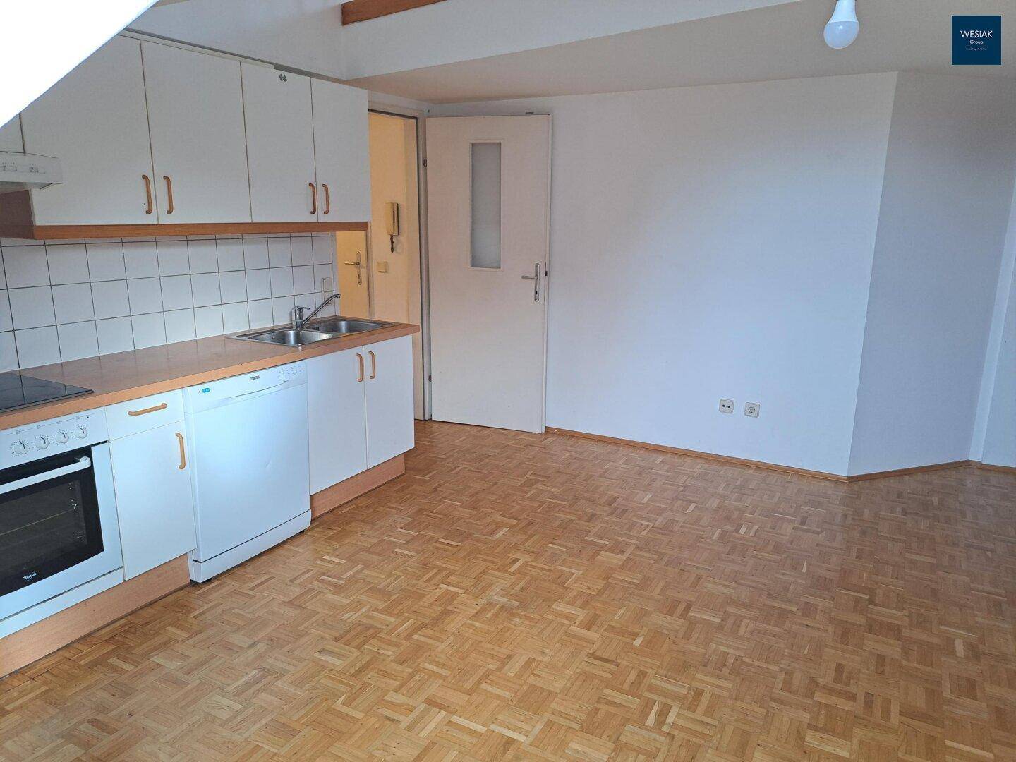 Funktionale Küche mit weißen Schränken und Parkettboden, offen zum angrenzenden Wohnbereich.