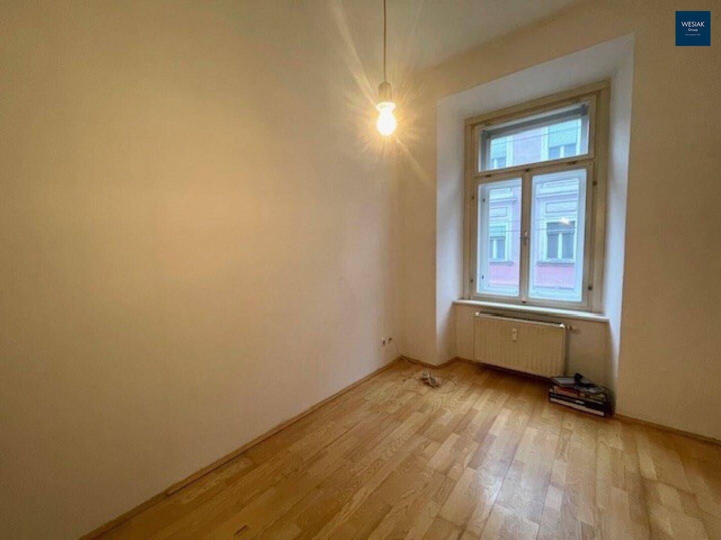 Helles Schlafzimmer mit Parkettboden und großem Fenster, bereit zur individuellen Gestaltung.