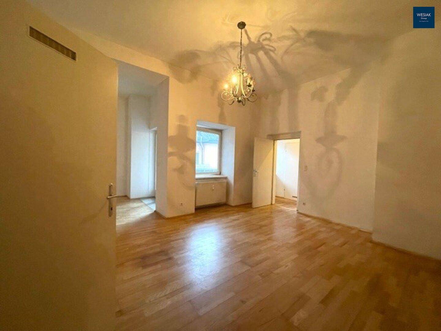 Helles Wohnzimmer mit Parkettboden, Kronleuchter und Zugang zu weiteren Räumen.