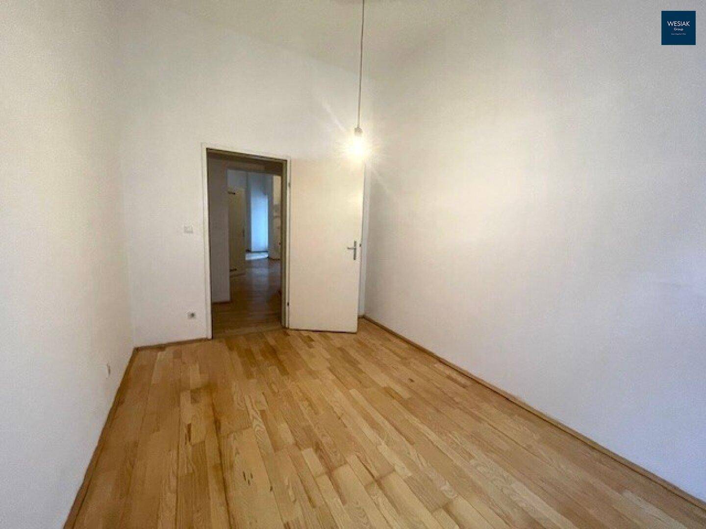 Leeres Schlafzimmer mit Holzboden und einfacher Beleuchtung, bietet viel Gestaltungspotenzial.