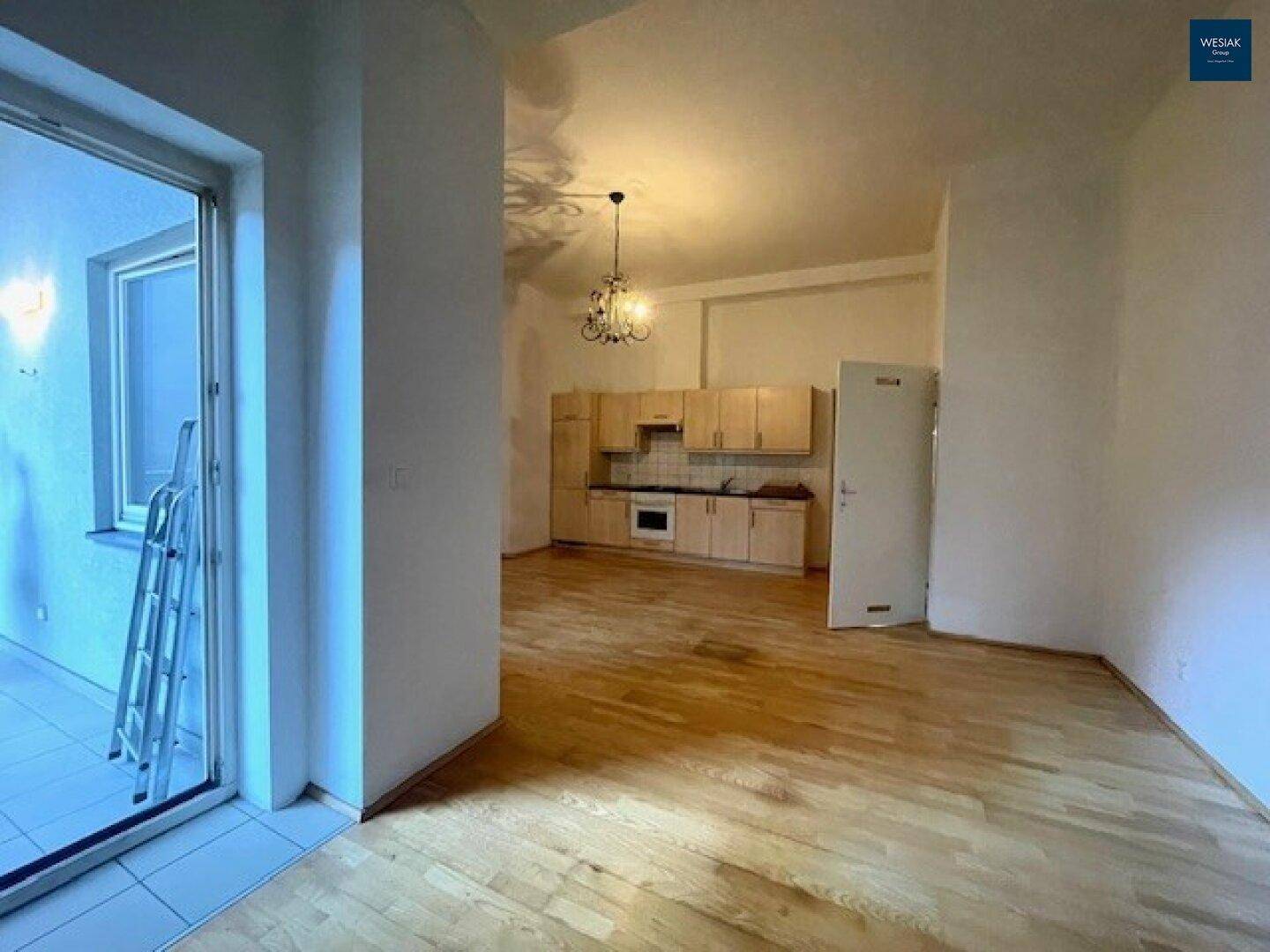 Offener Wohnbereich mit integrierter Küche, Parkettboden und Zugang zum Balkon.