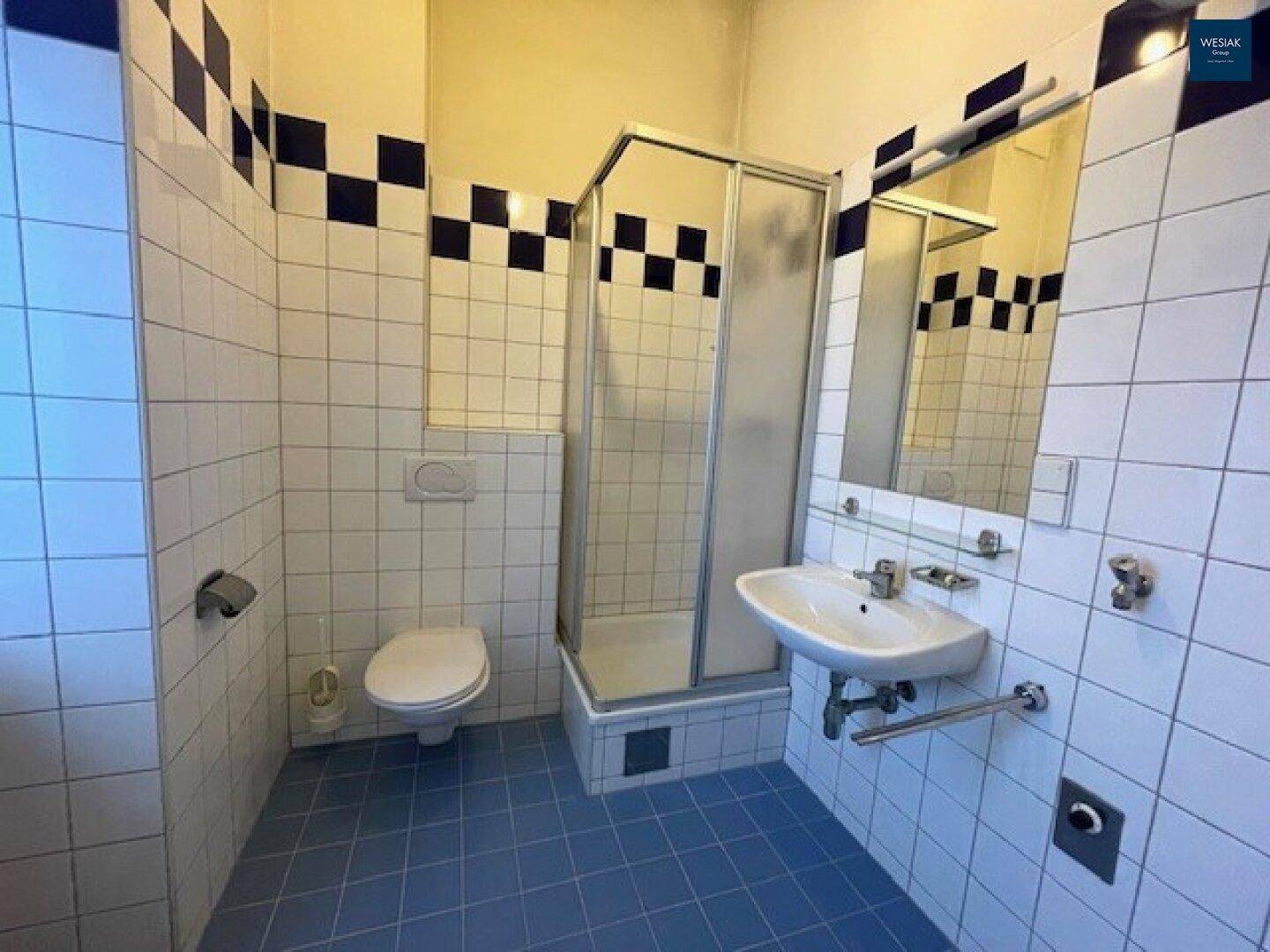 Badezimmer mit blauen und weißen Fliesen, Dusche, WC und Waschbecken.