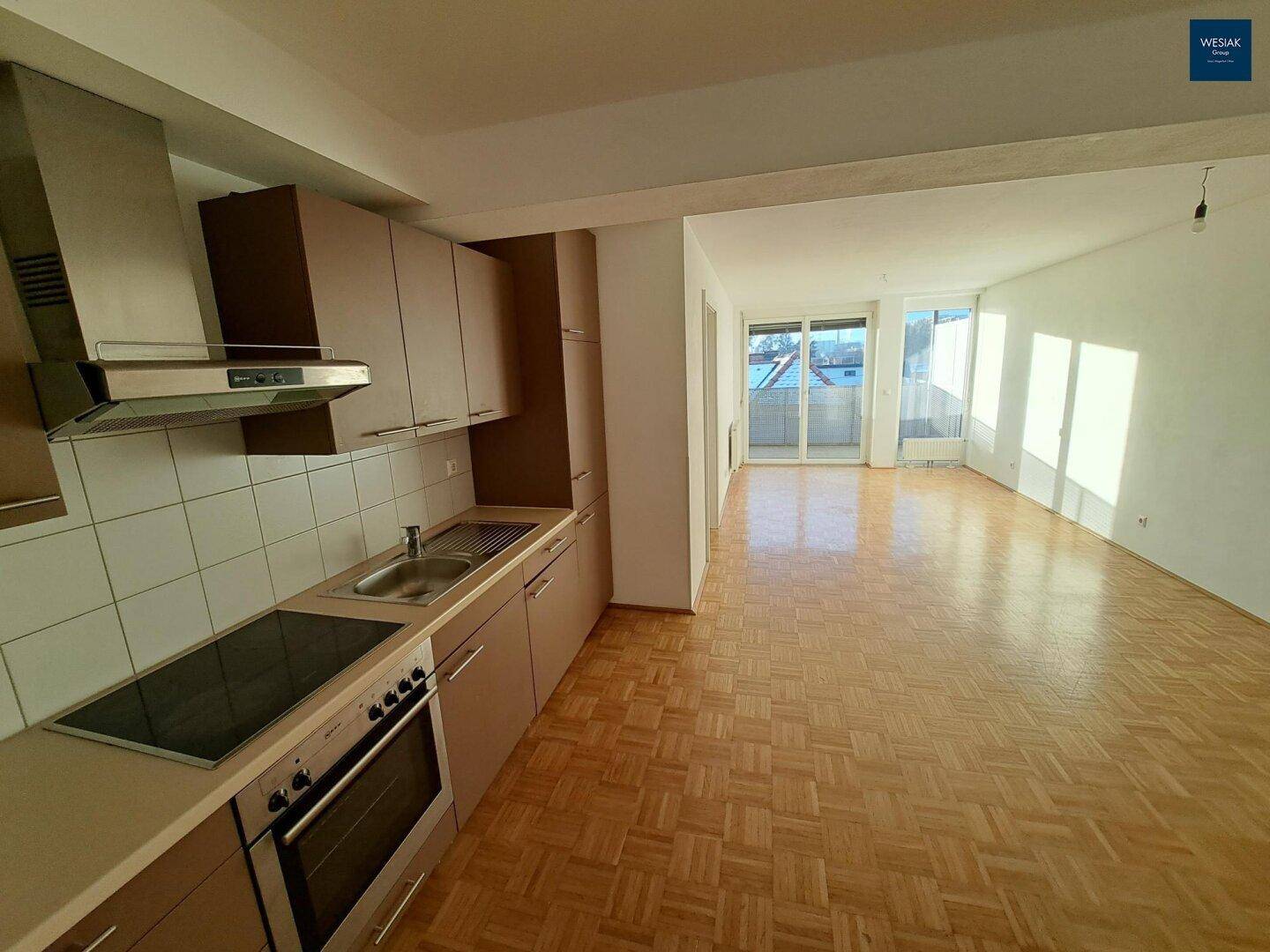 Funktionale Küche mit braunen Schränken und Parkettboden, offen zum hellen Wohnbereich.