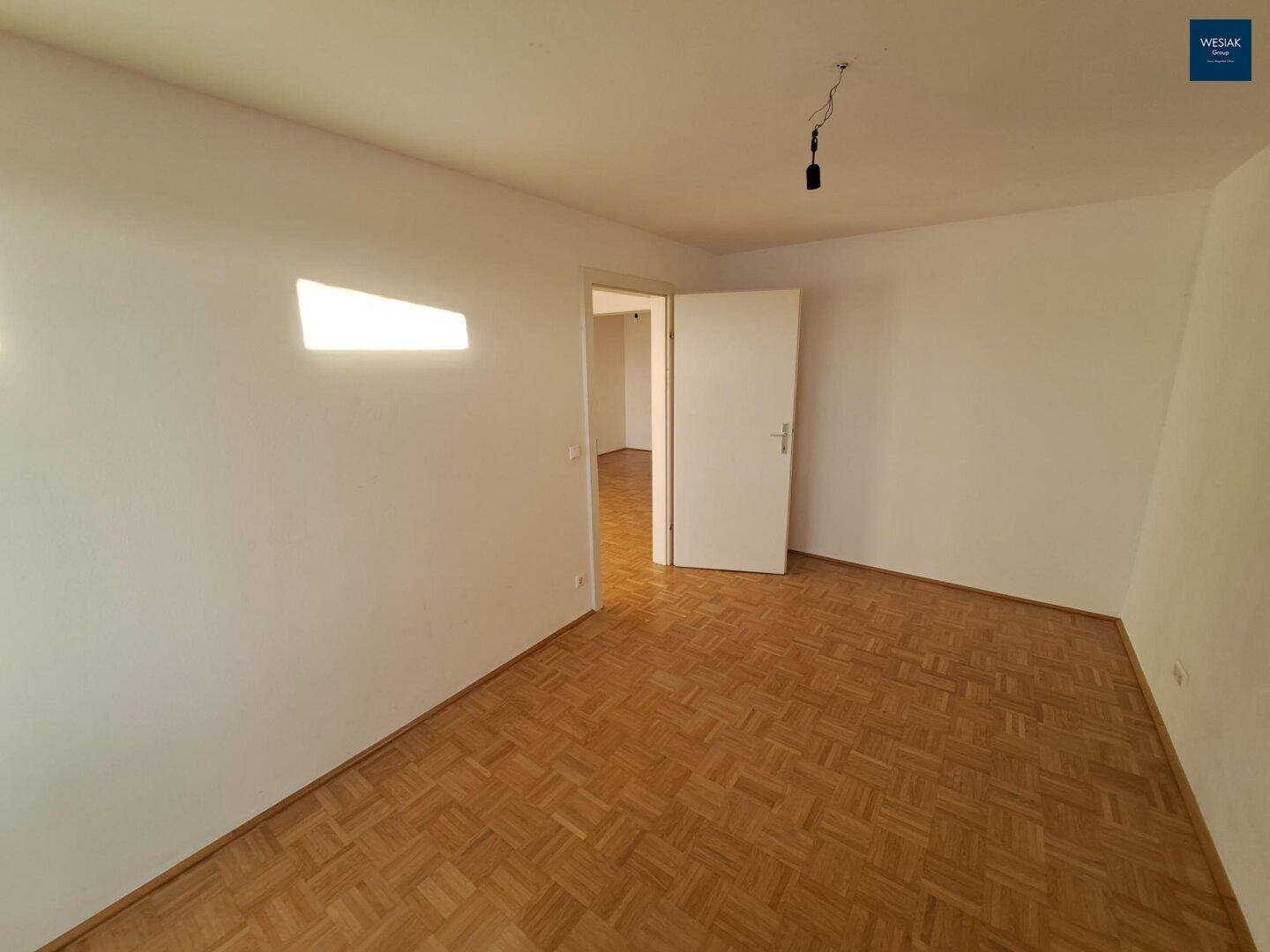 Leeres Zimmer mit Parkettboden und weiß gestrichenen Wänden, bereit zur individuellen Gestaltung.