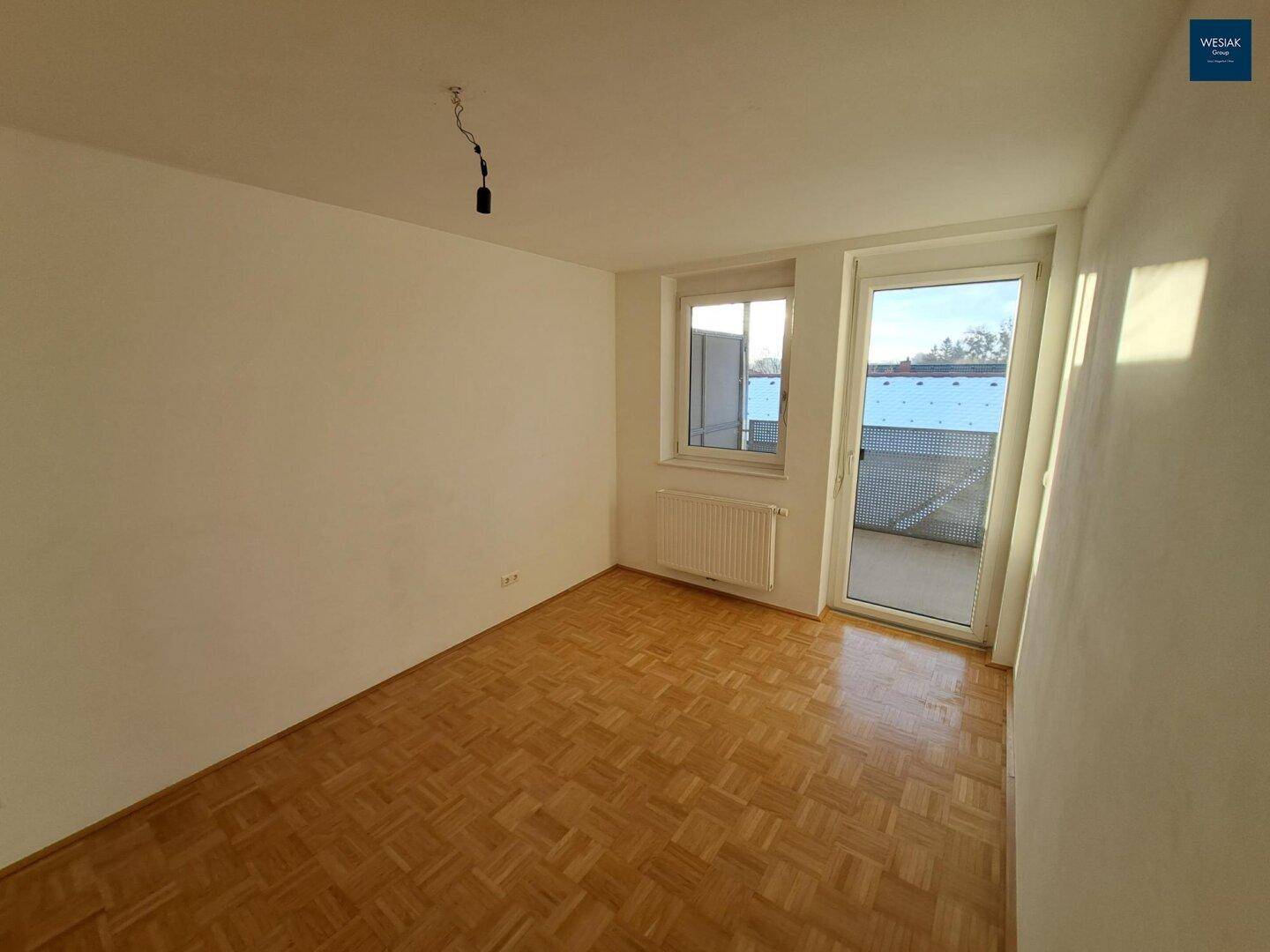 Helles Zimmer mit Parkettboden und direktem Zugang zu einem Balkon, ideal als Schlafzimmer.