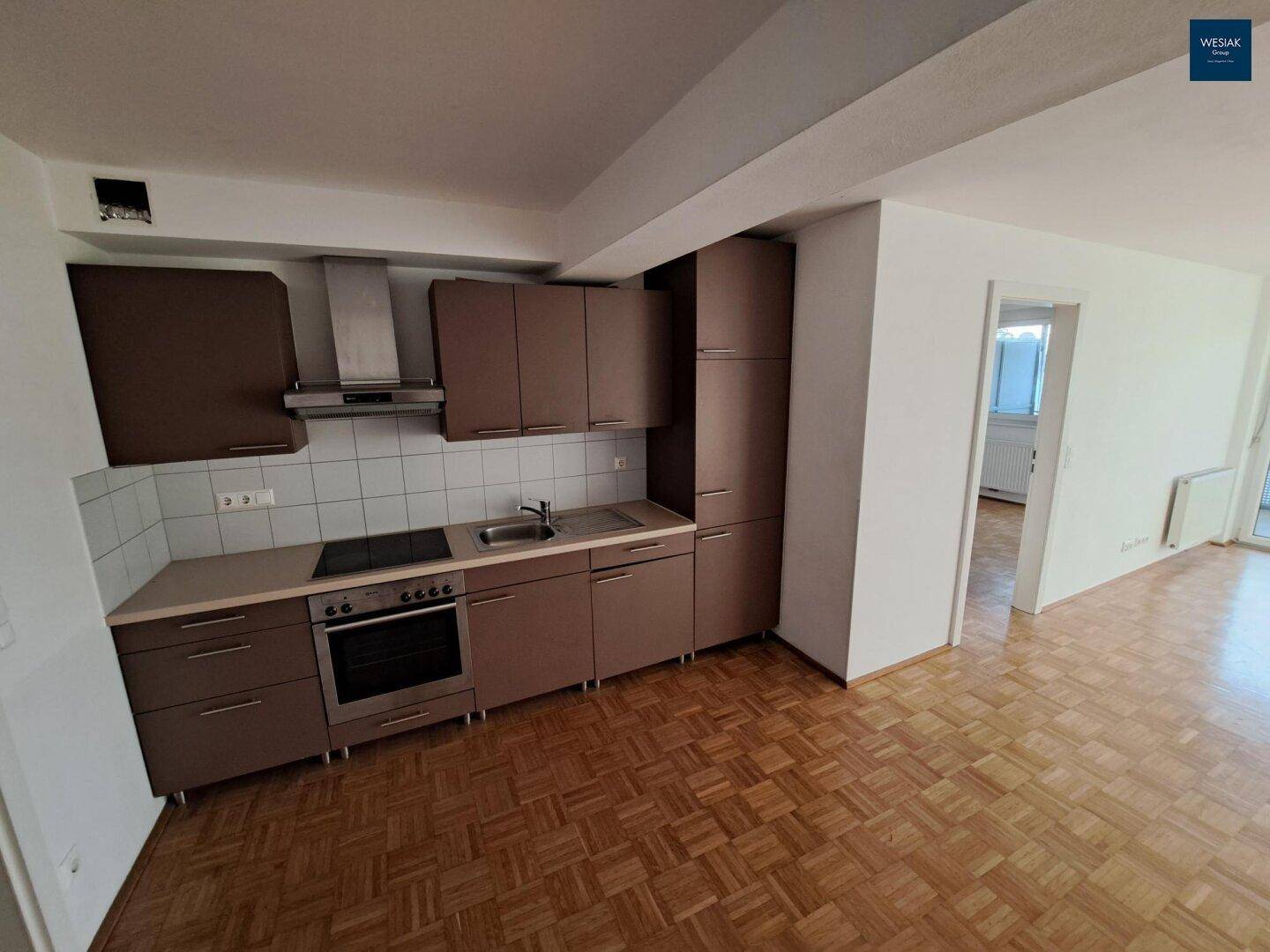 Einbauküche mit braunen Fronten und Parkettboden, offen zu angrenzenden Wohnbereichen.