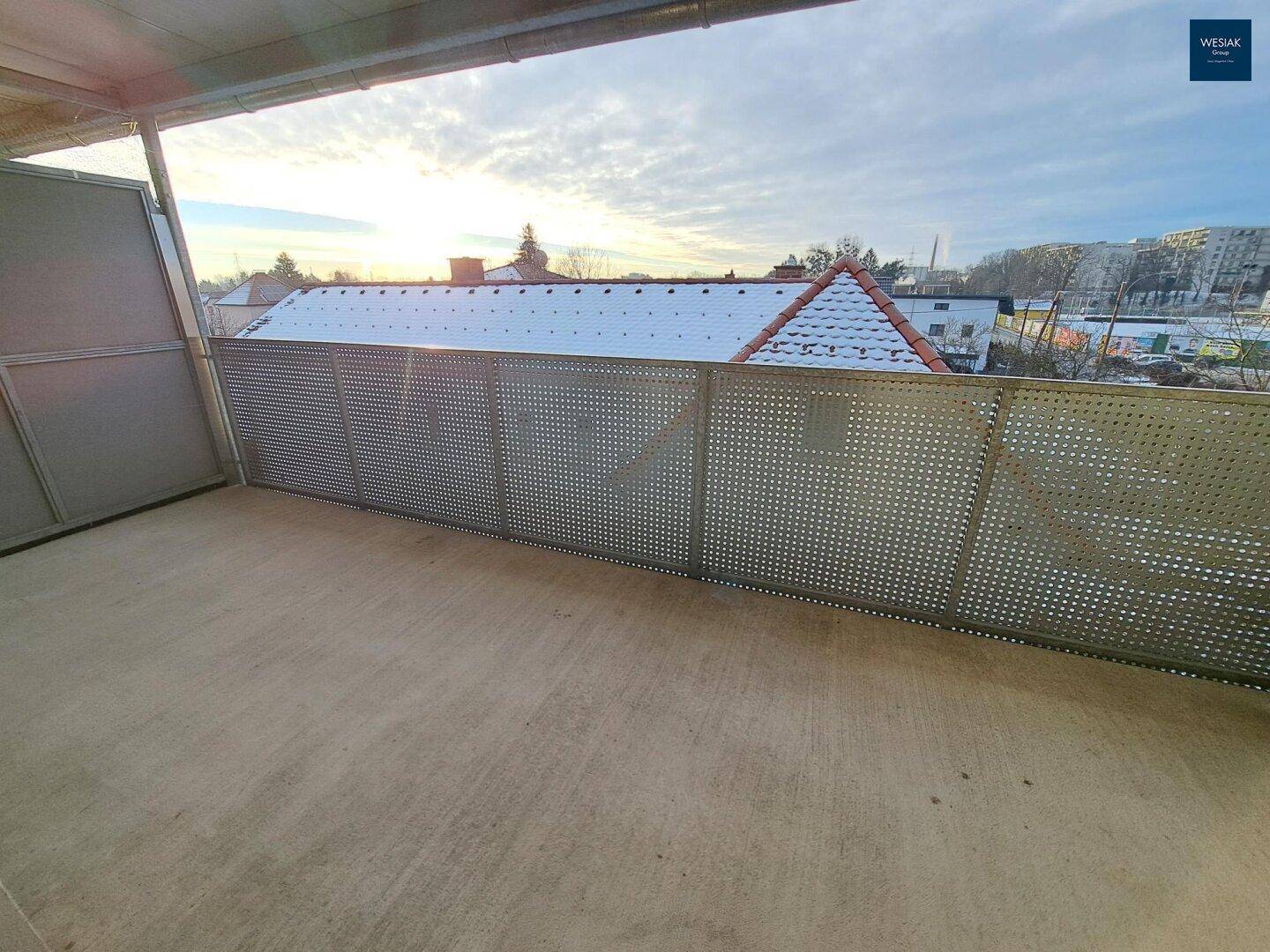 Leerer Balkon mit Metallgeländer und Blick über die verschneiten Dächer der Stadt.