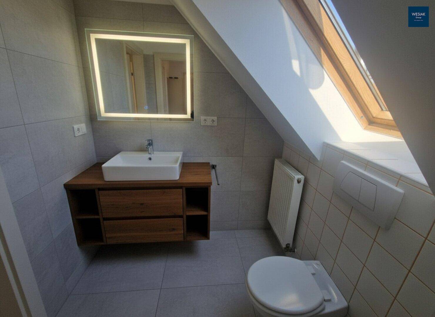Modernes Badezimmer im Dachgeschoss mit Waschtisch, WC und Oberlichtfenster.