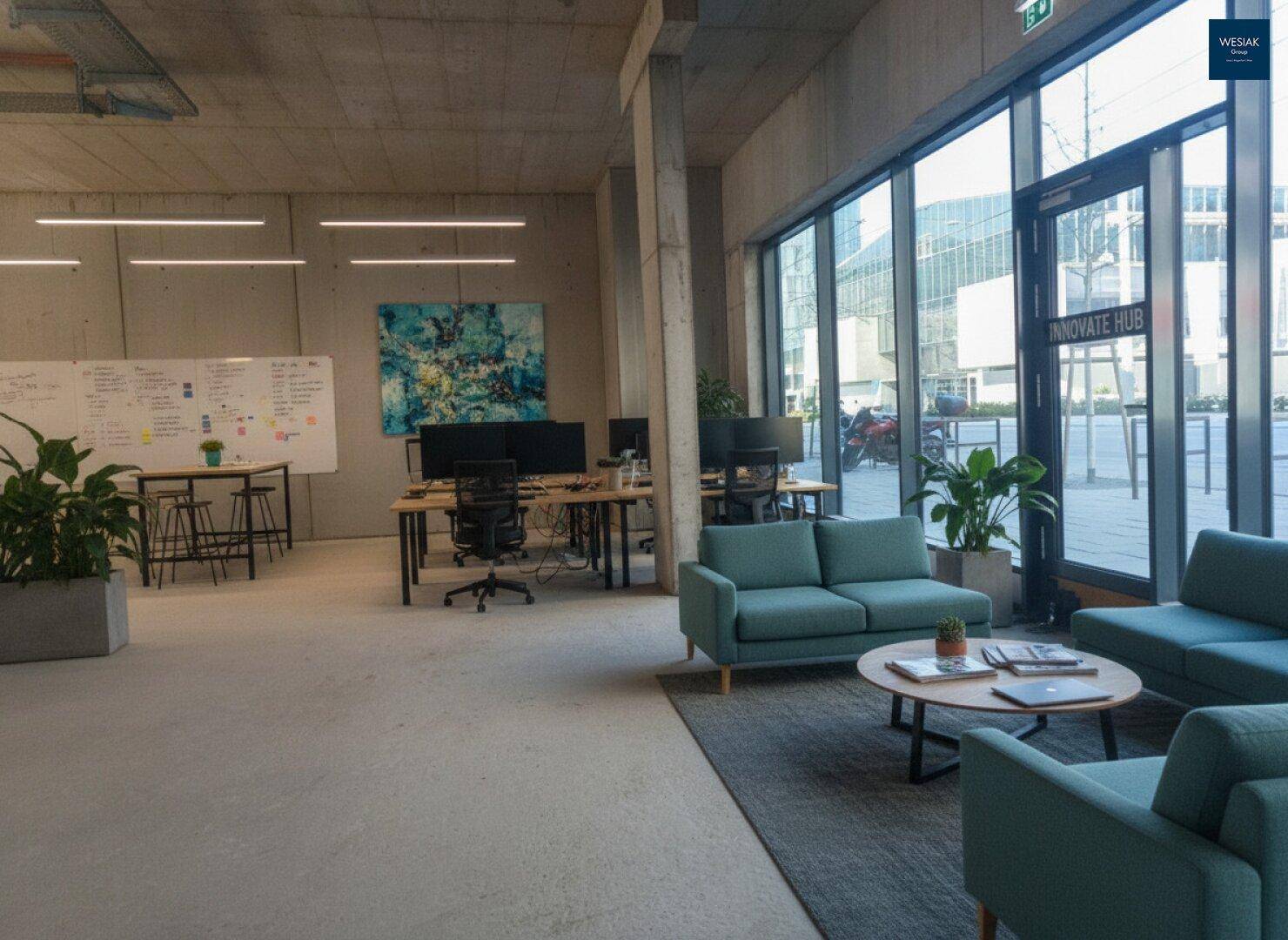 Offener Bürobereich mit Arbeitsplätzen, einer Lounge-Ecke und großen Fenstern für viel Tageslicht.