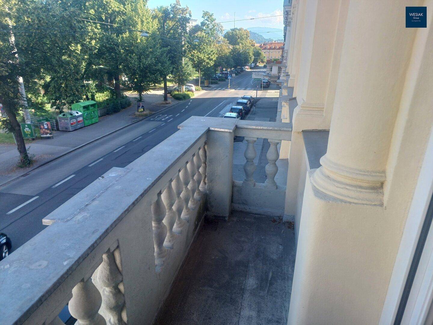 Kleiner Balkon mit Balustrade und Blick auf die belebte Straße und die umliegenden Bäume.