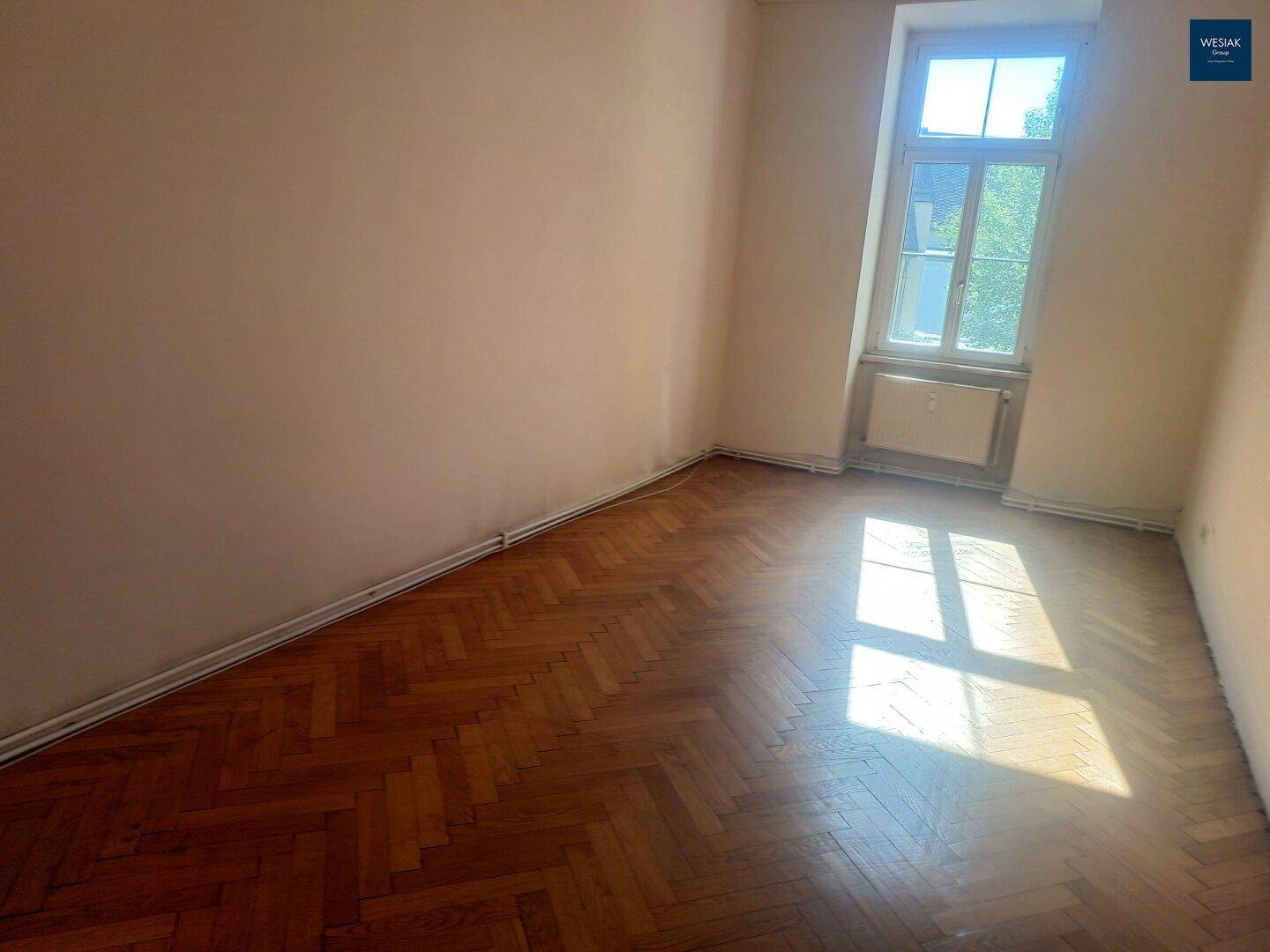 Kleineres Zimmer mit Fischgrätparkett und einem hohen Fenster, das den Raum mit Licht versorgt.