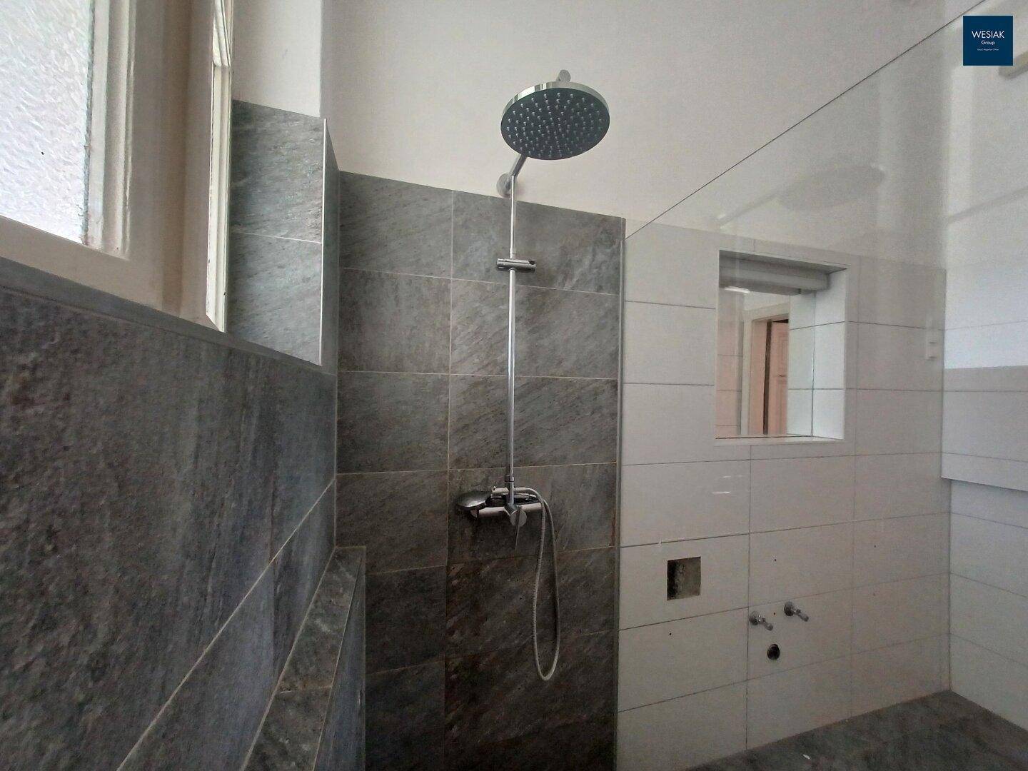 Moderne Duschkabine mit Regendusche und großformatigen Fliesen in Grau und Weiß.
