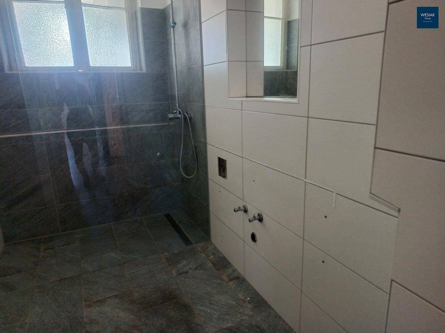 Geräumige Duschzone mit bodengleicher Dusche und modernen Fliesen, die ein helles Ambiente schafft.