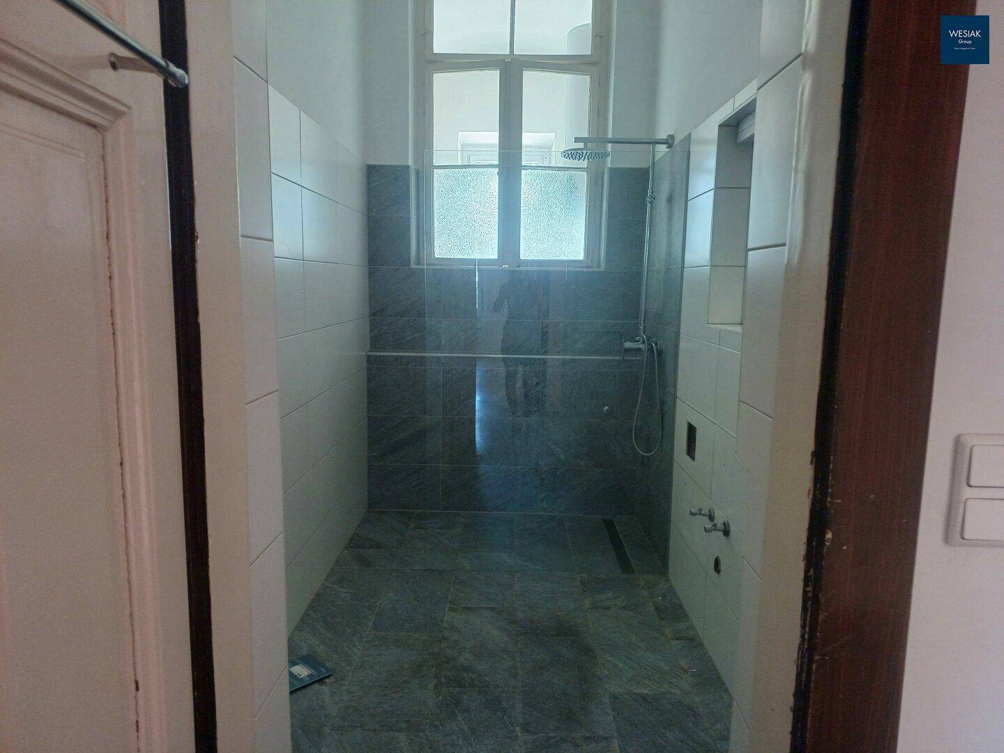 Offene Duschkabine mit Glaswand und Regendusche in einem modern gefliesten Badezimmer.