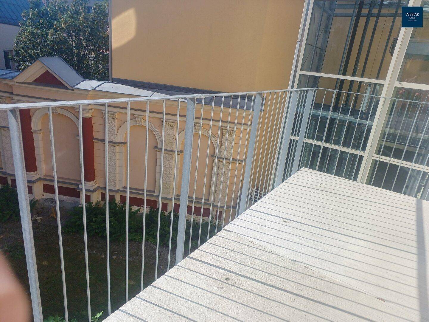Balkon mit Metallgeländer und Blick auf den Innenhofgarten und die historische Gebäudefassade.