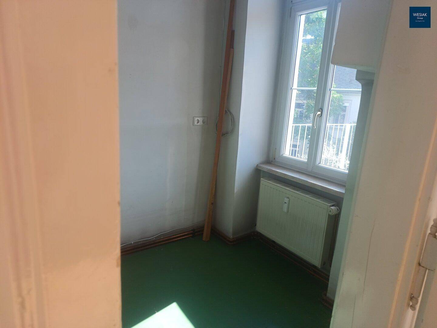 Kleiner Raum mit grünem Boden und einem Fenster, ideal als Abstellraum oder Speisekammer.