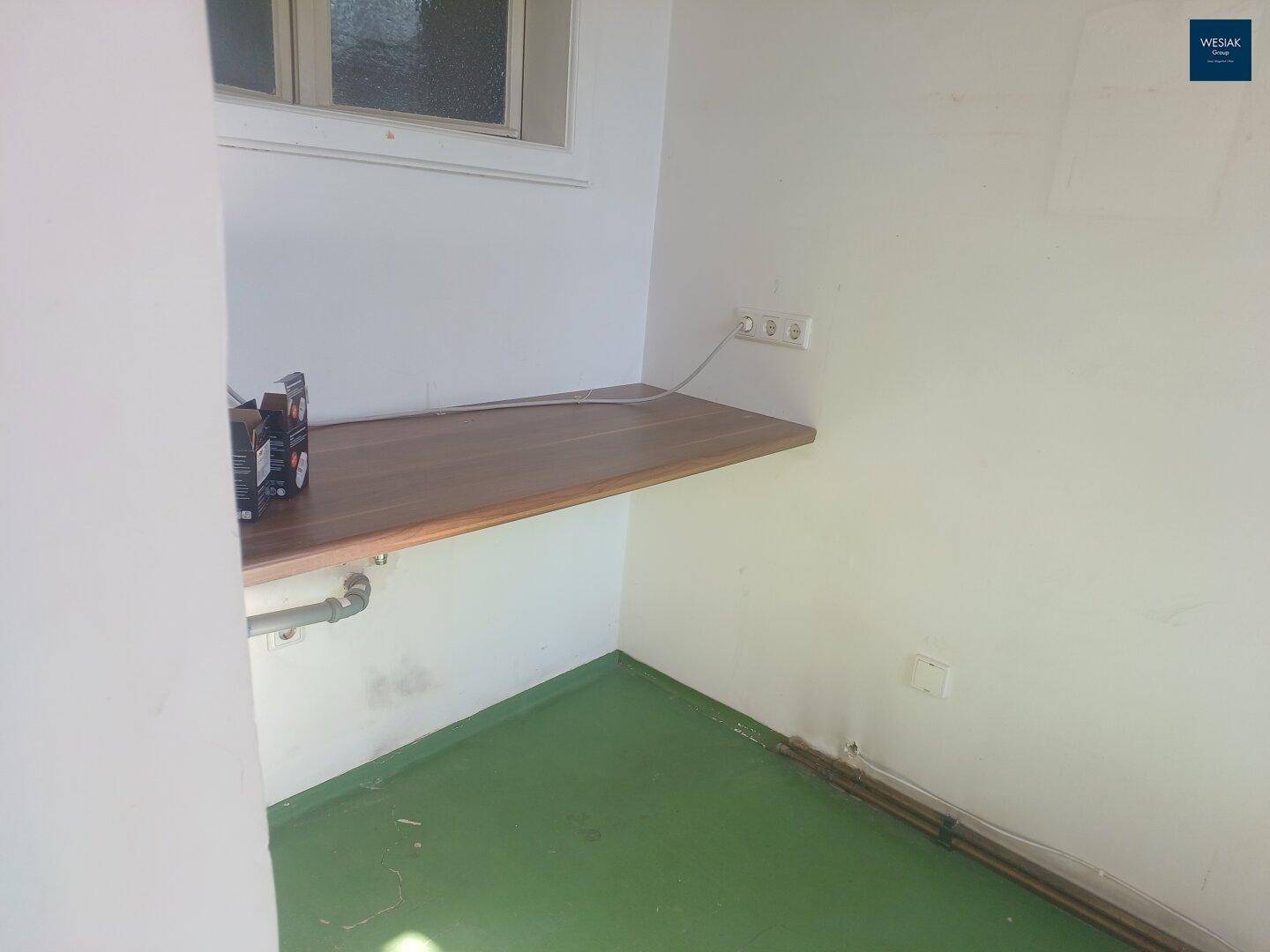 Einfacher Raum mit Arbeitsplatte und Fenster, geeignet als Waschküche oder Abstellkammer.