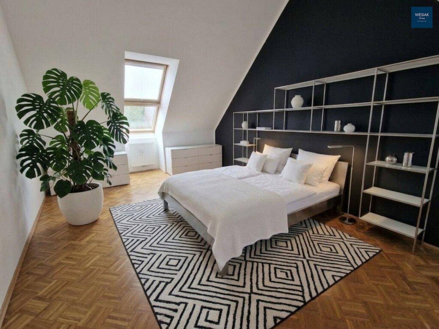 Modernes Schlafzimmer im Dachgeschoss mit Holzboden, dunkler Akzentwand und Dachfenster.