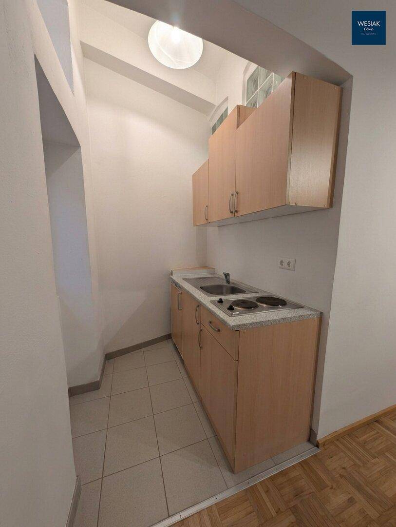 Kleine Küchenzeile mit zwei Kochplatten, Spüle und Holzschränken.