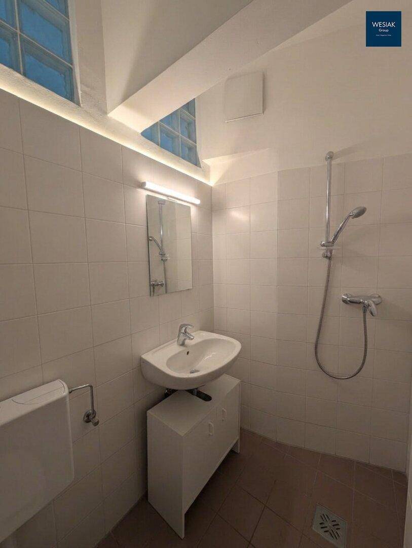 Funktionales Badezimmer mit weißen Fliesen, Waschbecken und Duschbereich.