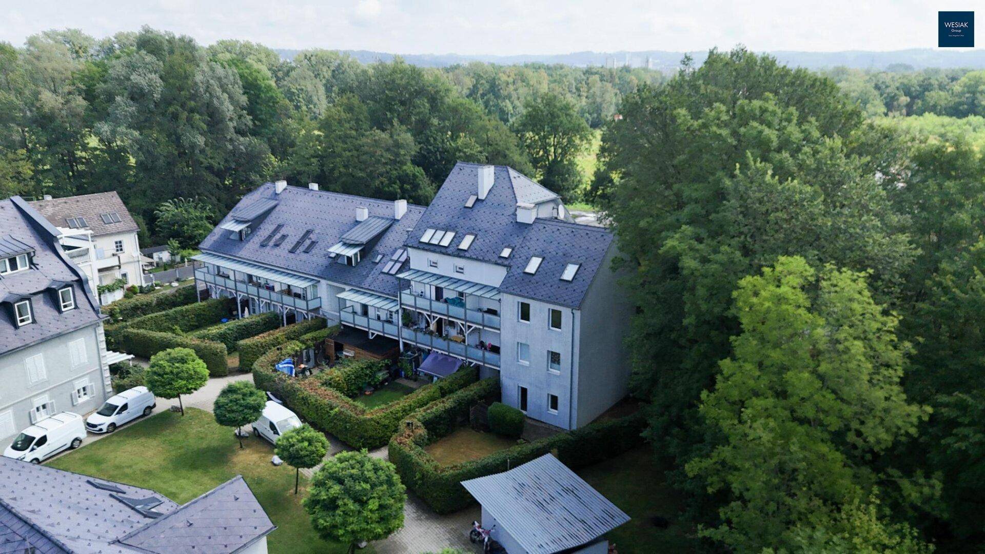 Luftaufnahme eines Wohngebäudes mit mehreren Balkonen und kleinen Gärten, umgeben von üppigem Grün.