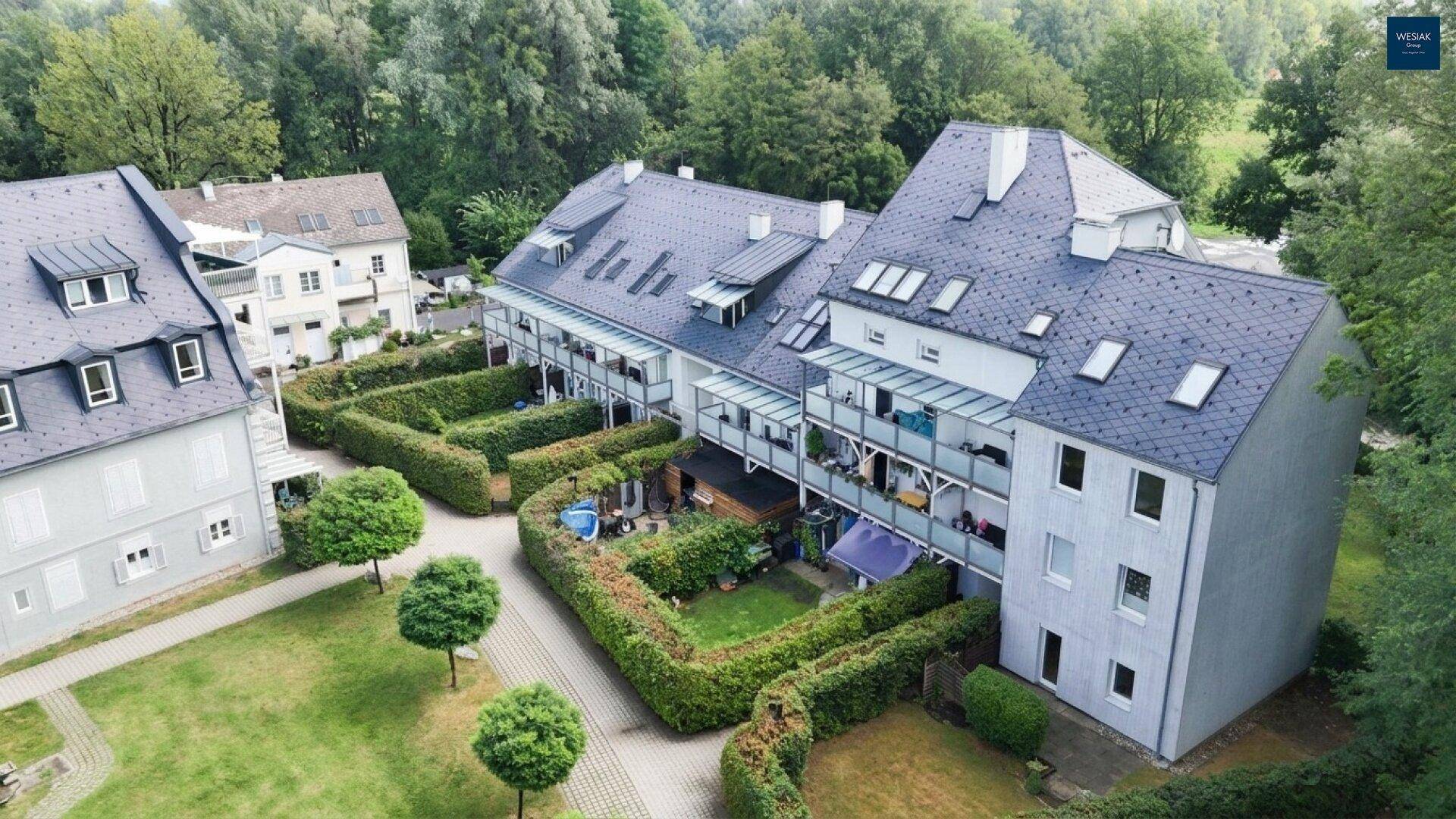 Luftaufnahme eines Wohnkomplexes mit Reihenhäusern, privaten Gärten und Balkonen, eingebettet in grüne Umgebung.