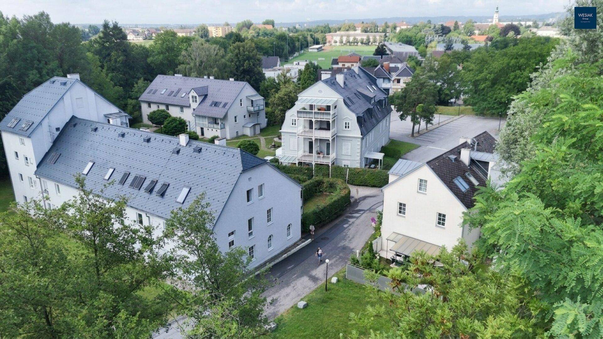 Luftaufnahme einer Wohnsiedlung mit mehreren Gebäuden, umgeben von viel Grün und Bäumen.