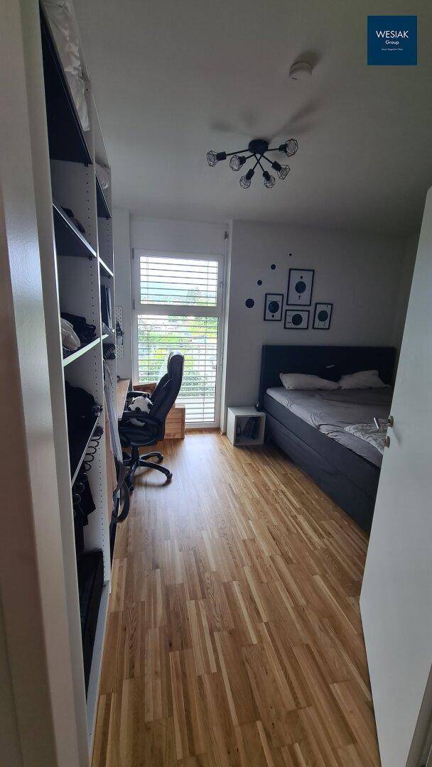 Helles Schlafzimmer mit Holzboden, großem Fenster und integriertem Arbeitsbereich.